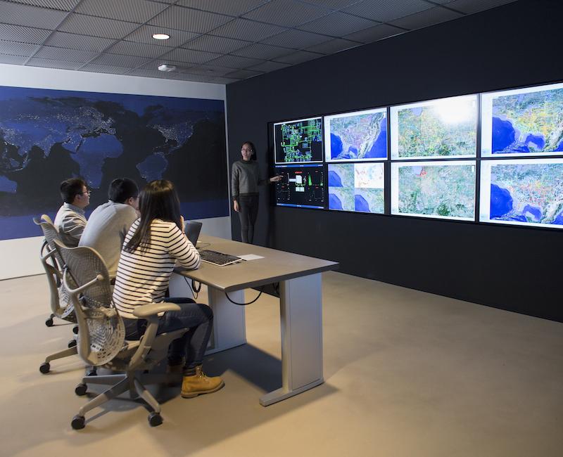 Photo of several people sitting at desk looking at screens with maps