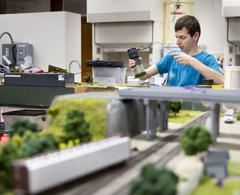 A student in the model railroad association lays grass on a model